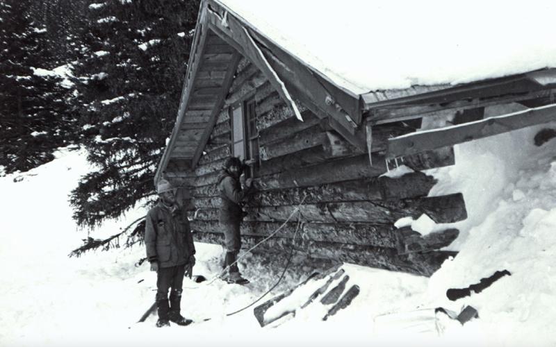 Avalanche damage at the Lizzie Deming Cabin in 1984. The cabin was hit by a slide on March 15, 1984, at about 8:15 p.m.. The cabin was built by Bill MacDougall and was purchased by Ben Barnes. Pictured are Chris George, left, and Art Mears in this photo taken by Don Bachman. They were investigating the slide for the county. San Juan County Historical Society photo