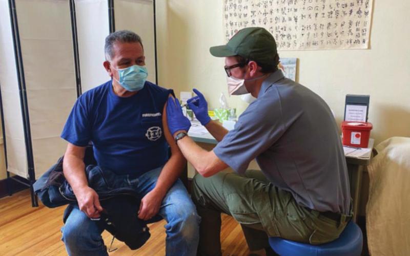 San Juan County Public Health made headlines for its COVID mitigation strategy that put the community first. Here Fire Chief Archuleta gets vaccinated by Ryan Copenhagen. Photo Credit SJCPHCutline
