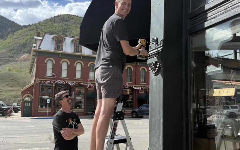 Shop owners Paul Joyce and Zach Dodge show teamwork in getting flags up on the Benson building in front of the Dodge General Store photo by DeAnne Gallegos