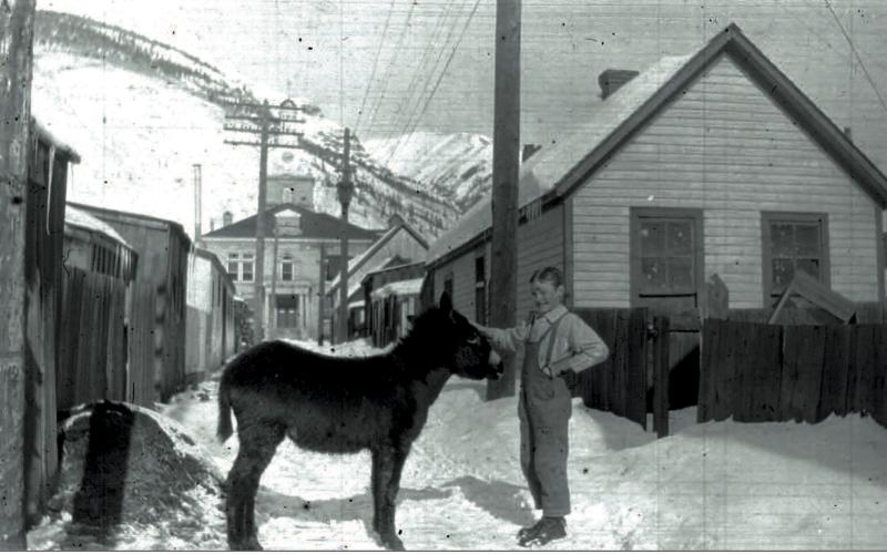 Denny McNaughton with a burro in the alley between Greene and Reese streets, with the San Juan County Courthouse behind them in 1917 or 1918. Photo courtesy of San Juan County Historical Society