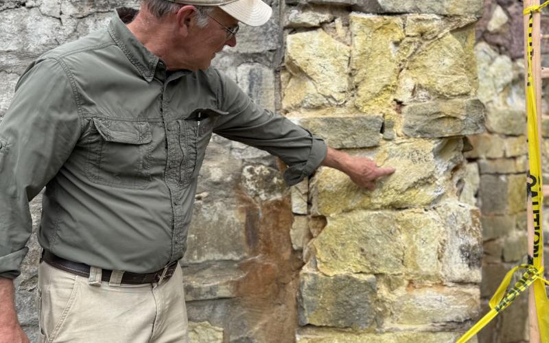 Geologist Ken Balleweg shows where the sulfuric process has started to deteriorate the stone wall behind the statue pedestal, this rock needs to be removed and replaced in order to stabilize the rock wall. Photo credit DeAnne Gallegos