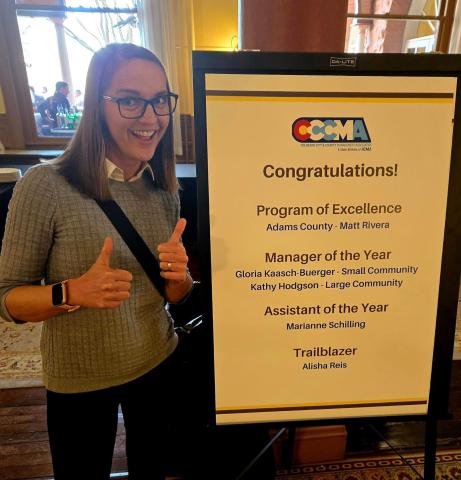 Town Administrator Gloria Kaasch-Buerger poses in front of the CCCMA conference sign that celebrated her big win in Glenwood. Photo credit Gloria Kaasch-Buerger