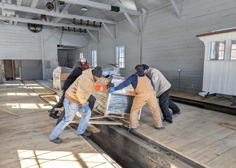 group of volunteers moves a pallet of Spacesaver shelving into storage jn the almost complete Silverton Northern Engine House. This is one of 12 pallets of materials of the units acquired for the Archinve. They will more than double the vault storage space available. As a side note, the picture also portrays the new look of the engine house interior, a welcome contrast to the dingy, poorly lit space of former days. On the right, can be seen the tail-end of the Society’s famous Casey Jones, snugly stored awa