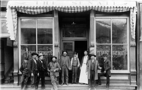 The front of The Senate Saloon in 1898 at 1239 Greene Street, with nine men in front, including bar tender Hi Washburn, in the doorway wearing an apron. San Juan County Historical Society photo