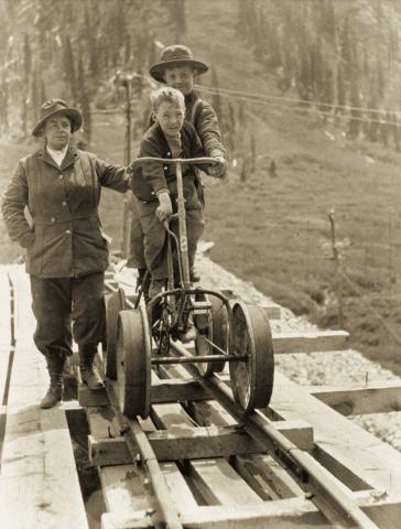A mine bicycle on mine rail in August 1914 at the Frisco Tunnel near Animas Forks. From left are Mrs. Henson, Fred Henson and Dan McNaughton Jr.