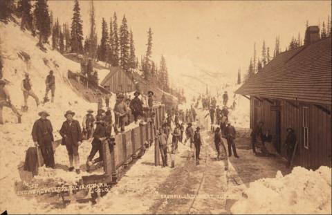 Track shovelers, likely returning from work, at the Red Mountain Town depot. The west face of the depot is at the right, with the main track by the platform and four cars on the western track. Image courtesy of: Judy Stine archives