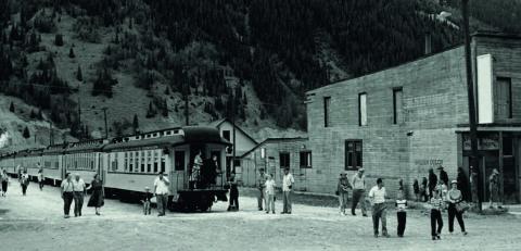 View down 12th Street on Aug. 1, 1955, as passengers disembark from the train. The National Hall building at right is now the vacant lot where the train comes in. In this photo it was lettered with “The Golden Gulch Saloon” for use as part of a movie set.