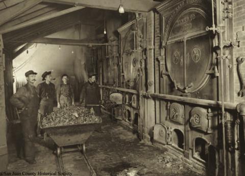 The main boiler room at the Gold King Mine in 1906. The photo shows three men around a coal car, and a fourth man shoveling coal into the firebox. The boiler tanks bear ornate endings, with the wording “the Gold King Consolidated Mines Co., 1900/Star Boiler Works.” Photo courtesy of San Juan County Historical Society