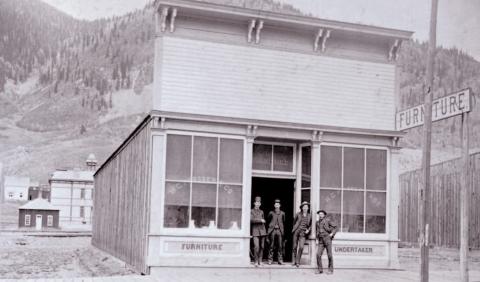 The Prosser Building at 1121 Greene Street was opened for business in June 1883, with Horace Greeley Prosser operating a furniture store and undertaker service. The building is next door to the Brown Bear Cafe. In the background can be seen the old wood-frame Silverton School which was built in 1884. Photo Courtesy of the San Juan Historical Society
