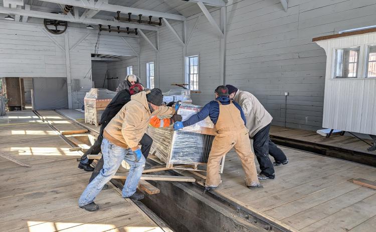 group of volunteers moves a pallet of Spacesaver shelving into storage jn the almost complete Silverton Northern Engine House. This is one of 12 pallets of materials of the units acquired for the Archinve. They will more than double the vault storage space available. As a side note, the picture also portrays the new look of the engine house interior, a welcome contrast to the dingy, poorly lit space of former days. On the right, can be seen the tail-end of the Society’s famous Casey Jones, snugly stored awa