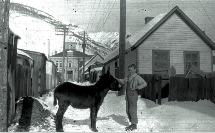 Denny McNaughton with a burro in the alley between Greene and Reese streets, with the San Juan County Courthouse behind them in 1917 or 1918. Photo courtesy of San Juan County Historical Society