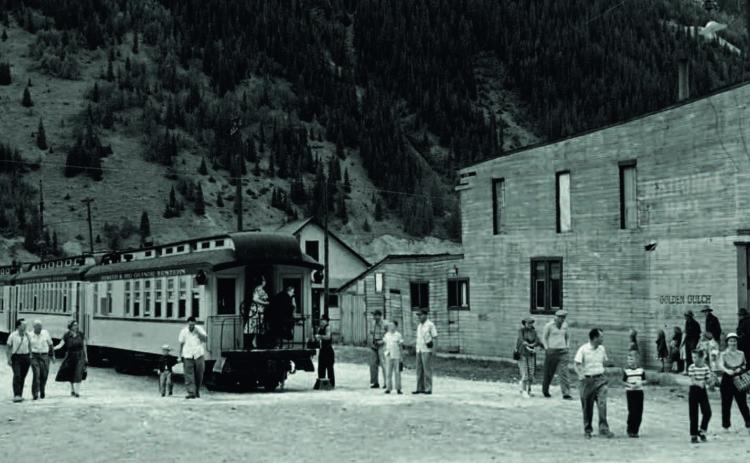 View down 12th Street on Aug. 1, 1955, as passengers disembark from the train. The National Hall building at right is now the vacant lot where the train comes in. In this photo it was lettered with “The Golden Gulch Saloon” for use as part of a movie set.